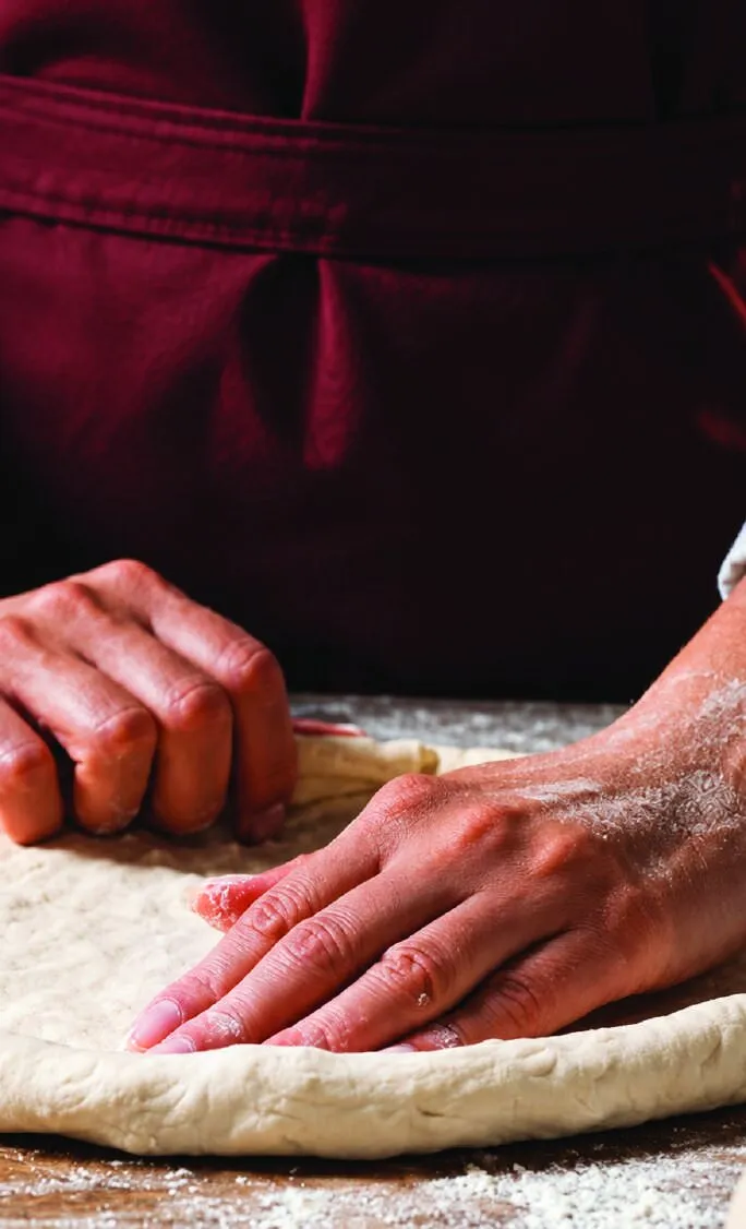 Hands stretching pizza dough at By The Chef